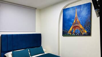 A bedroom with a bed, a headboard, and a painting of the Eiffel Tower.