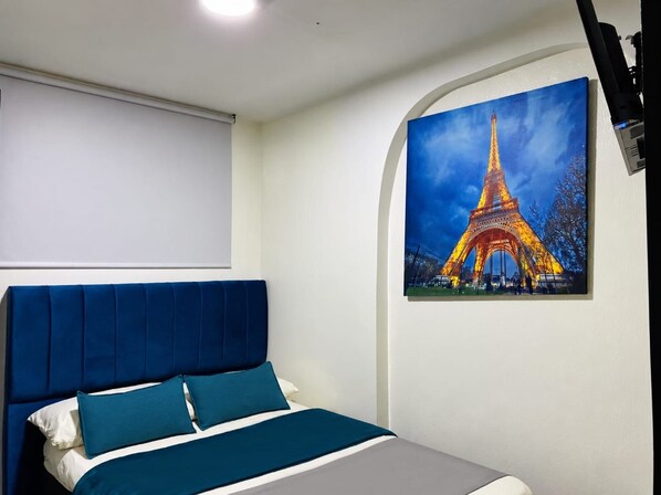 Un dormitorio con cama, cabecera y una pintura de la Torre Eiffel.