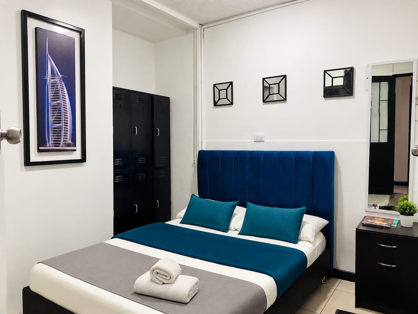 Een hotelkamer met een bed, een kledingkast, een spiegel en een ingelijst schilderij aan de muur.