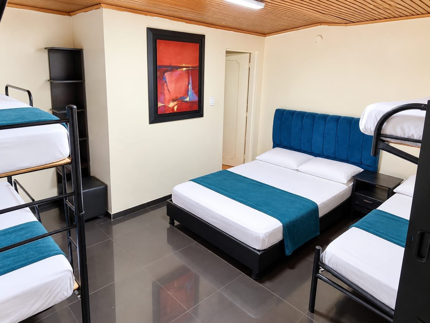 Een hotelkamer met stapelbedden, een nachtkastje, een lijst met een kunstwerk aan de muur en een deur naar de aangrenzende kamer.