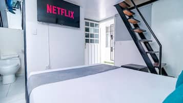 Quarto de hotel moderno com cama, TV na parede, escada e porta para o exterior.