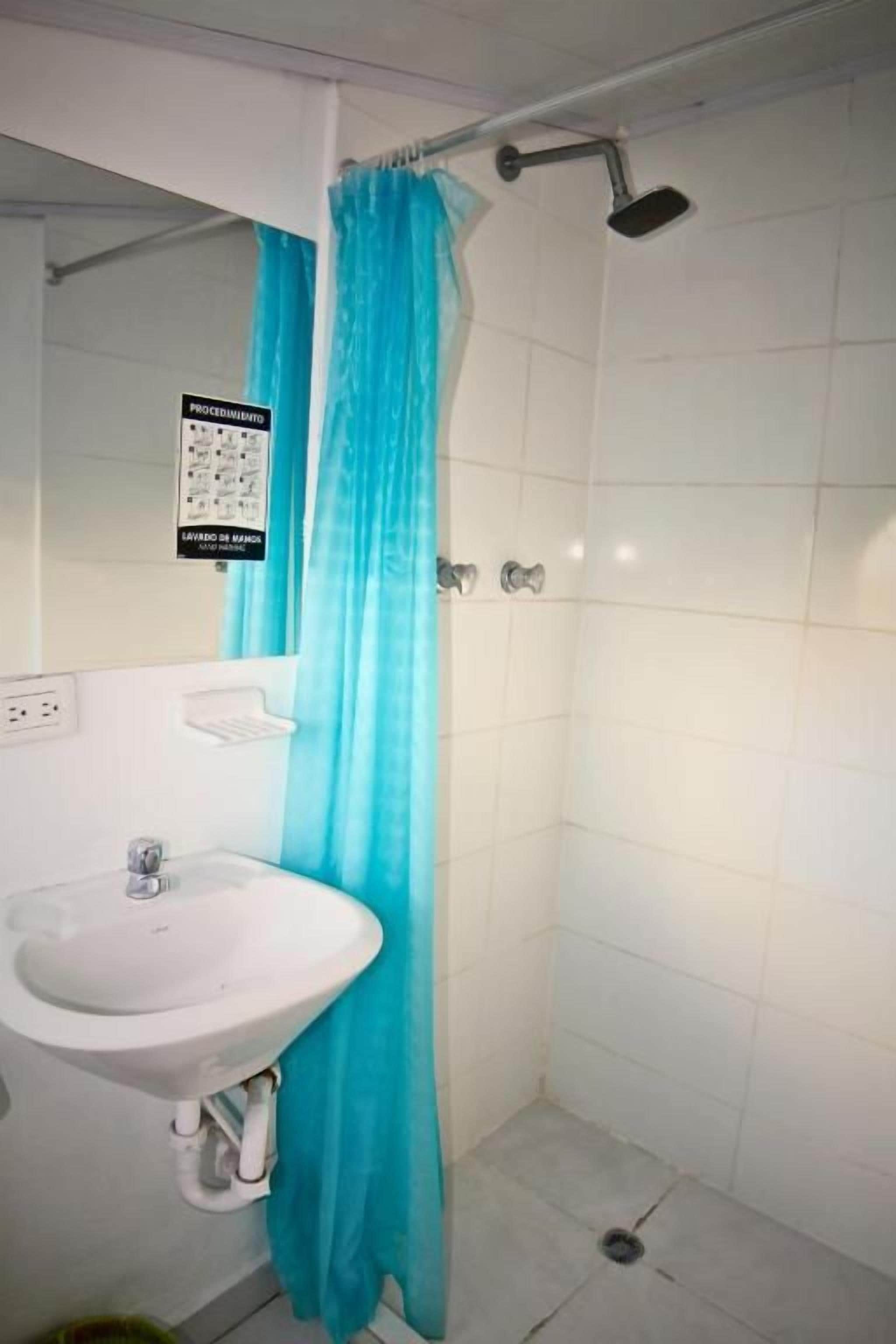 Un baño con un lavamanos blanco, una ducha con cortina azul y un letrero en la pared.