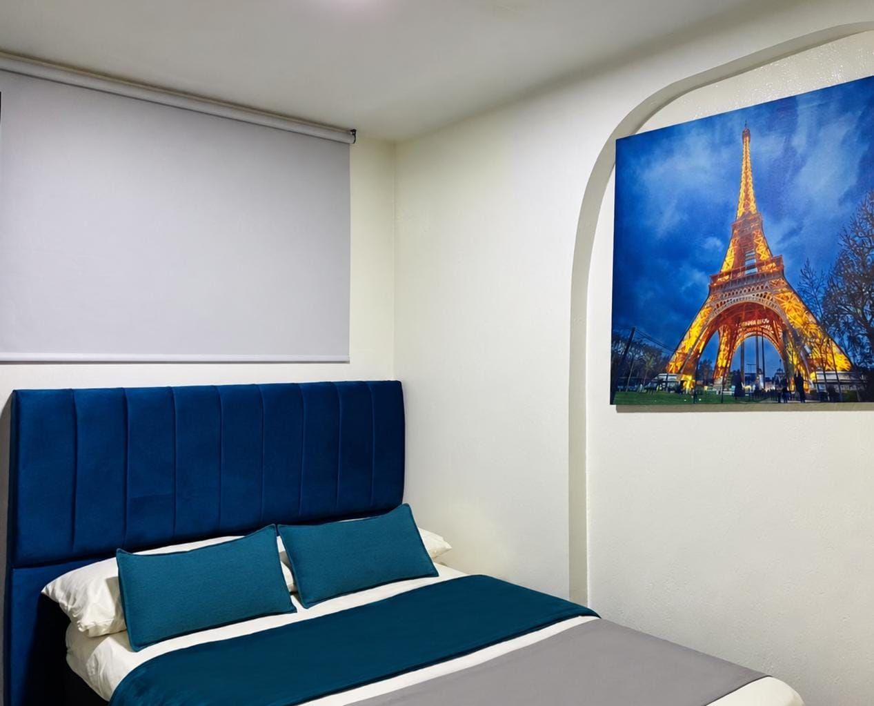 Een slaapkamer met een bed, een hoofdeinde en een schilderij van de Eiffeltoren.