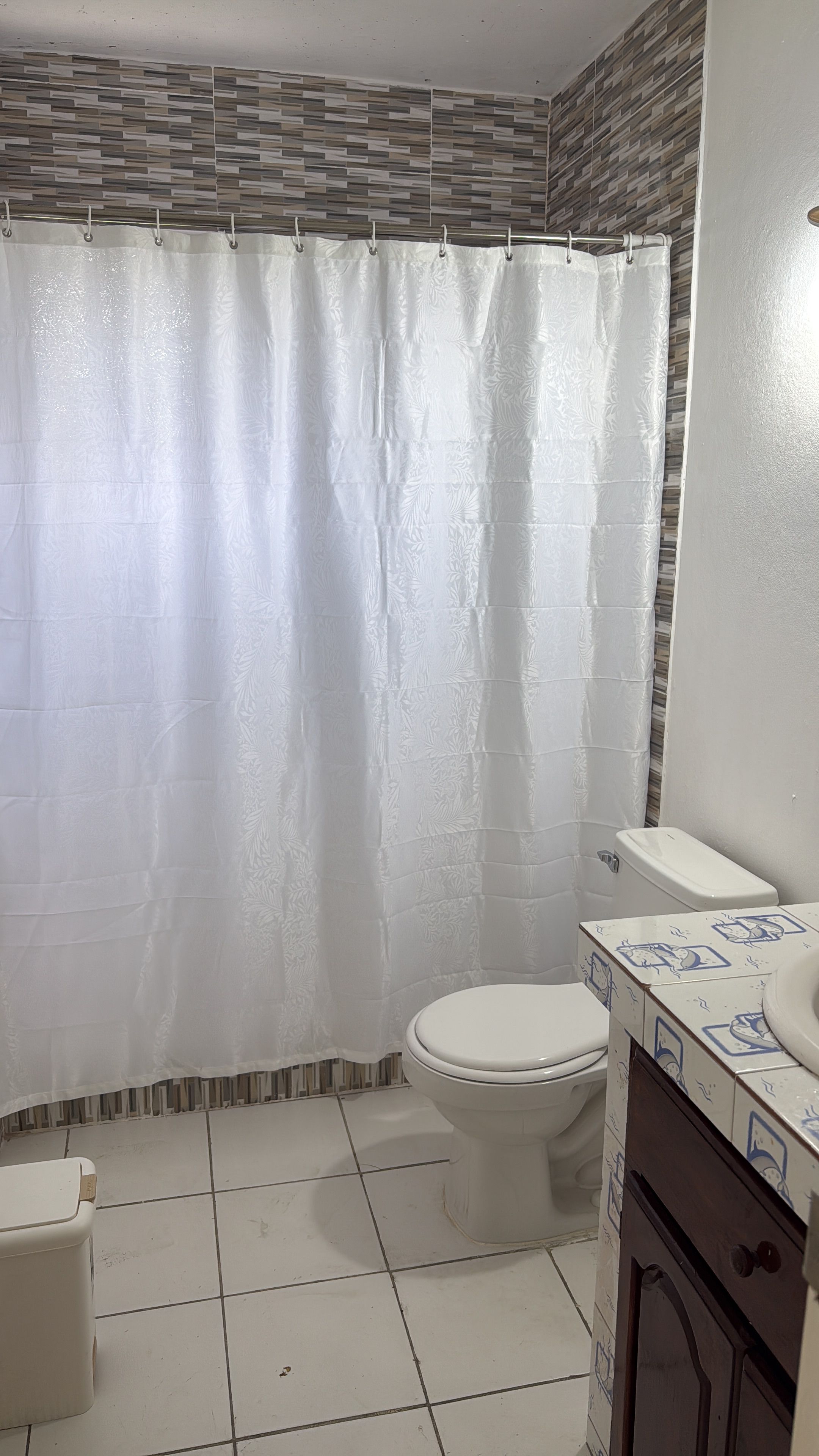 A bathroom with a shower curtain, toilet, and tiled floor.
