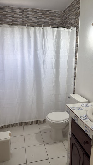 A bathroom with a shower curtain, toilet, and tiled floor.