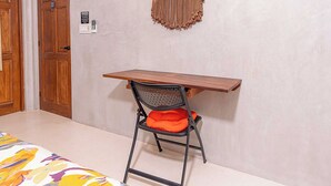 Ein Zimmer mit einem Holztisch, einem schwarzen Netzstuhl mit orangefarbenem Kissen und einer Wandleuchte.