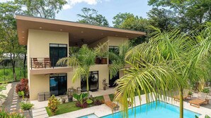 Ein modernes, zweistöckiges Haus mit Swimmingpool, Gartenmöbeln und üppiger Bepflanzung.