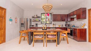 A modern kitchen with a central island, wooden chairs, a chandelier, and built-in wooden cabinets. - 8BR/4BA AC House in Playa Grande, 4 Min Walk to the Beach, Pool, Rancho, Parking (Playa Grande)