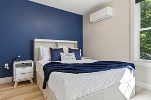 Une chambre à coucher comprenant un lit, une table de chevet et un climatiseur fixé au mur.