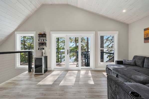A spacious room with a sloped ceiling, a large sliding glass door leading to a deck, a built-in bench, and a sofa with a cushion.