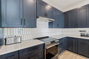 Una cocina moderna con armarios azul oscuro, una estufa de acero inoxidable y un respuesto de azulejos.