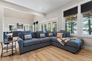 A modern living room with a sectional sofa, a coffee table, and a view of a lake through large windows.