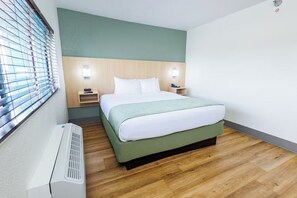Ein Hotelzimmer mit einem Bett, Nachttischen, einem Heizgerät und einem Fenster mit Jalousien.