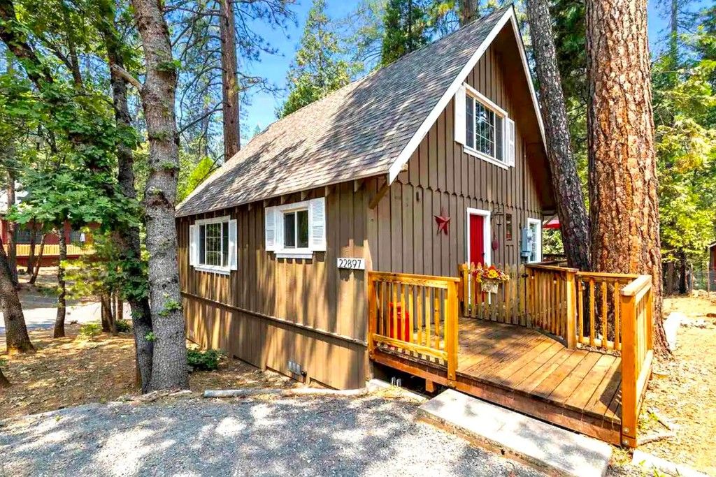 A wooden cabin with a porch, surrounded by trees.