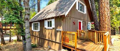 A wooden cabin with a porch, surrounded by trees.