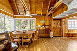 A cabin interior with a dining table, chairs, a sofa, a ceiling fan, and a 'Welcome to the Cabin' sign. - Red Door Cottage. Close to town! Pet-friendly! (Twain Harte)