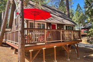 A wooden cabin with a deck, a red umbrella, and a rustic exterior. - Red Door Cottage. Close to town! Pet-friendly! (Twain Harte)