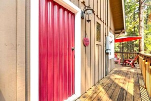 Um deck de madeira com uma porta vermelha, uma placa de boas-vindas e área de estar externa.