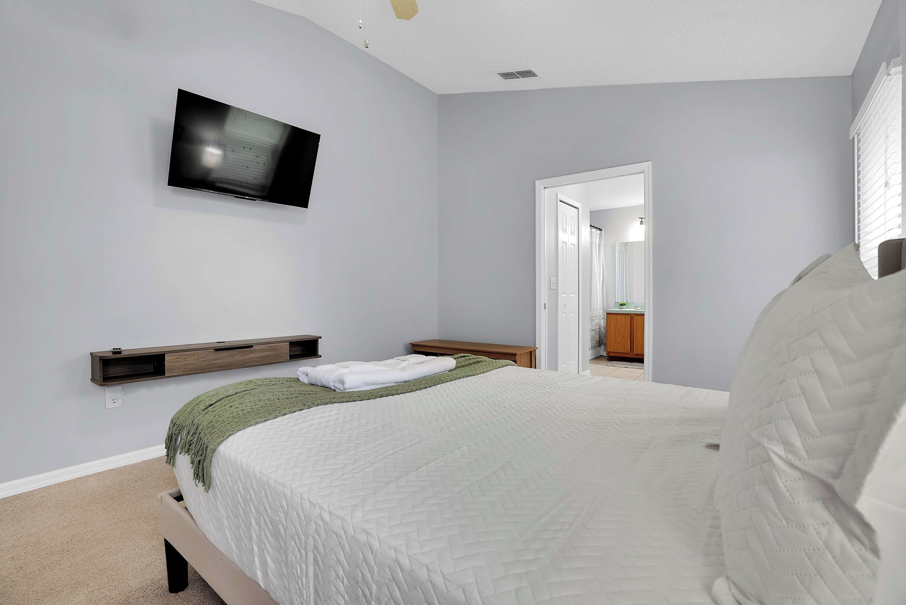 A bedroom with a bed, a television mounted on the wall, and a door leading to a bathroom.