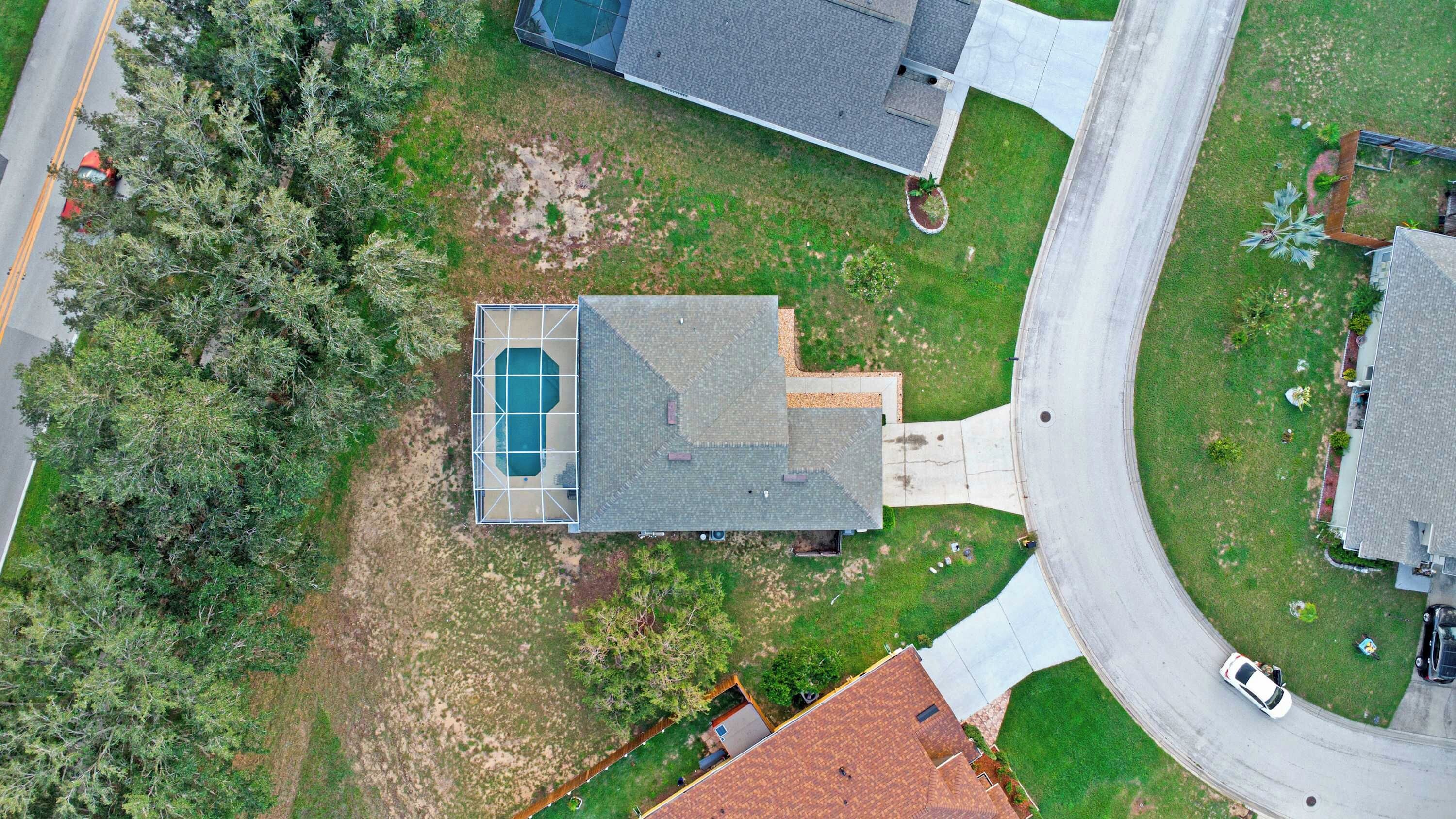 An aerial view of a residential property with a swimming pool, a driveway, and a road nearby.