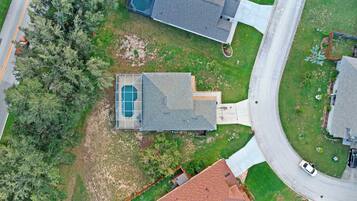 An aerial view of a residential property with a swimming pool, a driveway, and a road nearby.