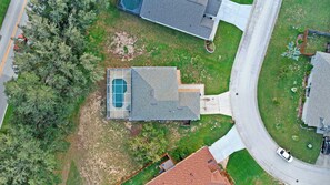 An aerial view of a residential property with a swimming pool, a driveway, and a road nearby.