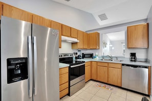 A modern kitchen with stainless steel appliances, wooden cabinets, and a tiled floor.
