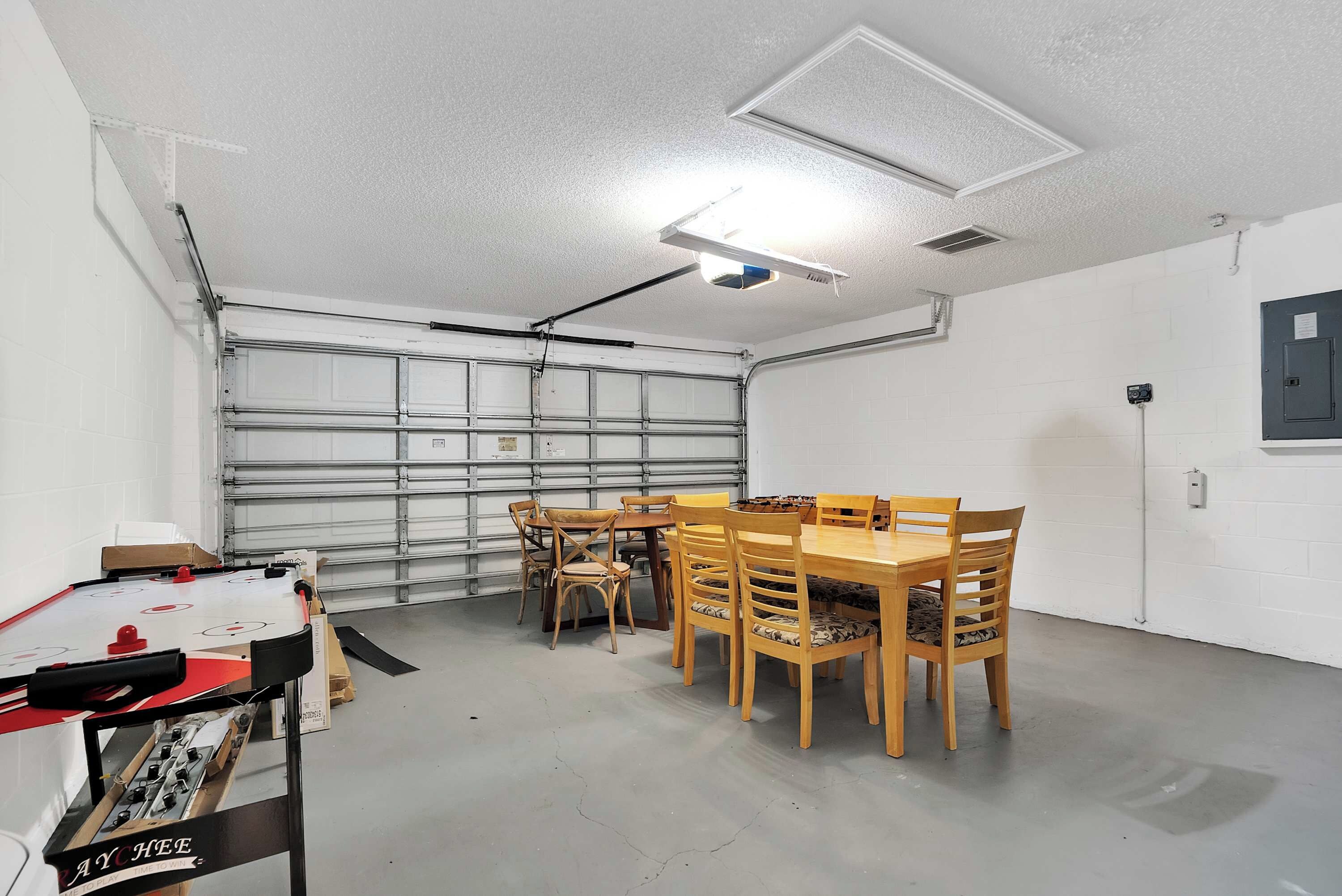 A garage with a dining table and chairs, a foosball table, and a ceiling light.