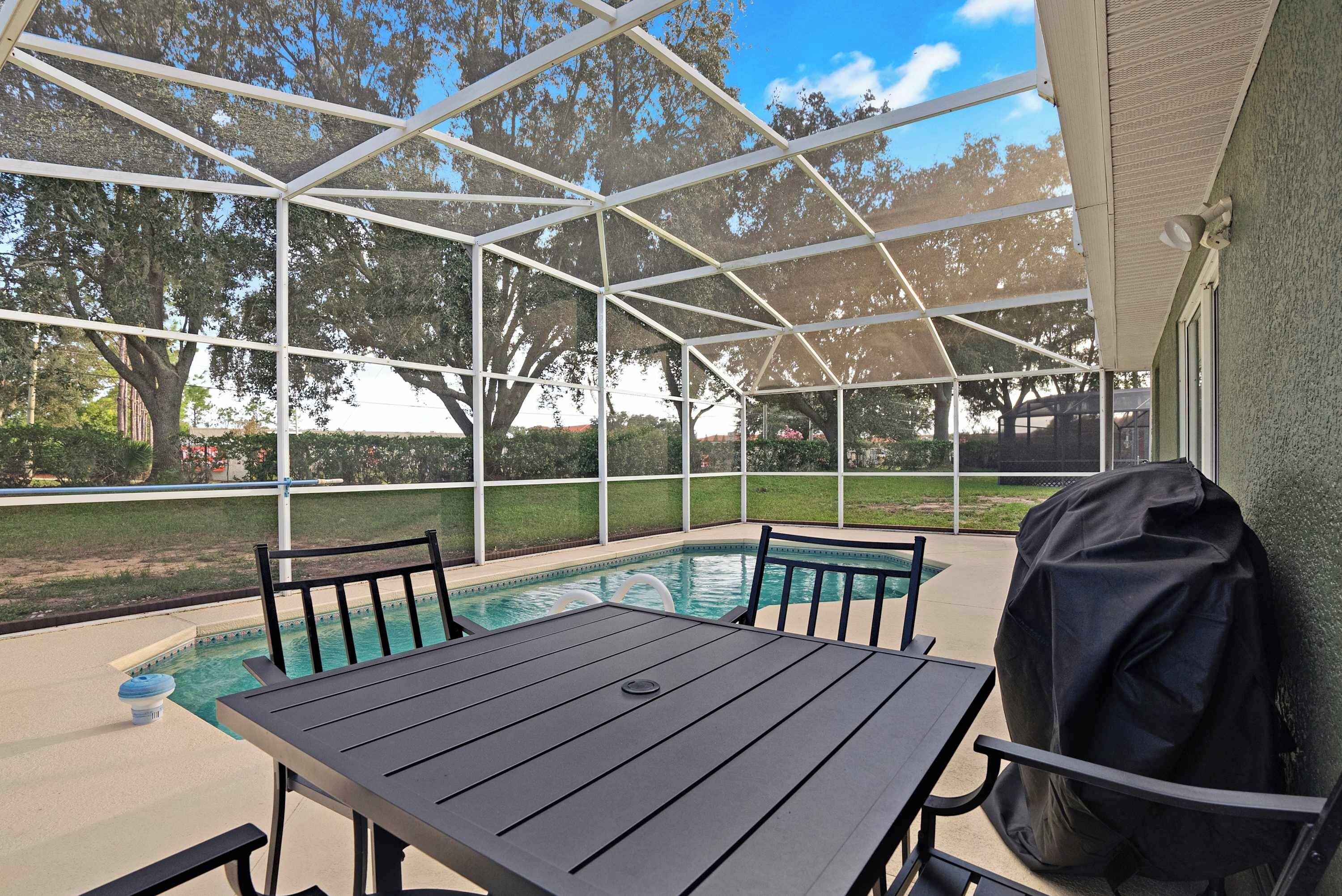 An outdoor pool area with a covered seating area and a grill.