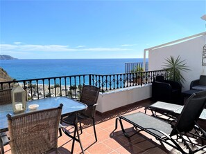 Eine Terrasse mit Meerblick, möbliert mit Korbstühlen und Tischen, und einem Geländer.
