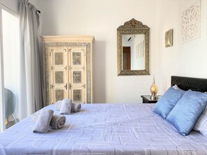 Ein Schlafzimmer mit Bett, Nachttisch, Spiegel, Kleiderschrank und einem Fenster mit Vorhängen.