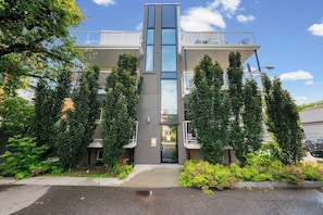 Un bâtiment moderne avec une entrée centrale, entouré de verdure et sous un ciel dégagé.