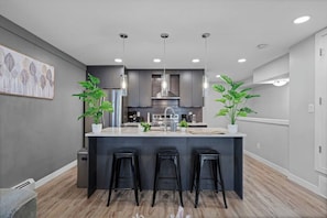 A modern kitchen with a central island, bar stools, stainless steel appliances, and pendant lighting. - Upscale 2BR/2BA Apt | Mins to NAIT, MacEwan & DT - Apartment (Edmonton)
