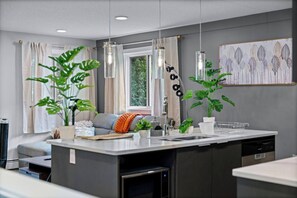 Une cuisine moderne avec un îlot central, des luminaires suspendus et des plantes en pot.
