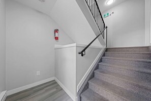 A staircase with a handrail, a fire extinguisher mounted on the wall, and a light fixture above. - Upscale 2BR/2BA Apt | Mins to NAIT, MacEwan & DT - Apartment (Edmonton)