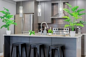 Une cuisine moderne dotée d’appareils électroménagers en acier inoxydable, d’un îlot central avec des tabourets et de luminaires suspendus.