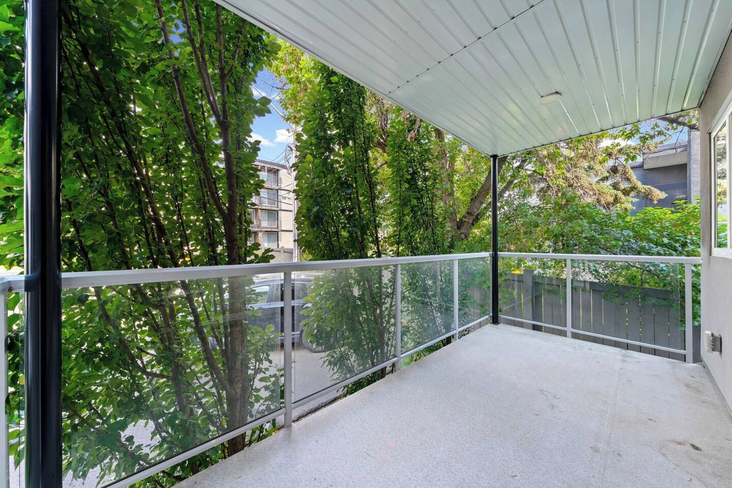 Un balcon doté d’une rambarde en métal, entouré d’arbres et avec un bâtiment visible au loin.