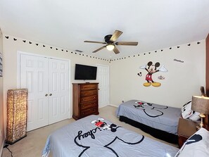 A bedroom with two beds, a ceiling fan, a TV, and Mickey Mouse decals on the walls. - Luxury 5BD 3.5BA Pool Home in Windsor Palms Resort (Kissimmee)