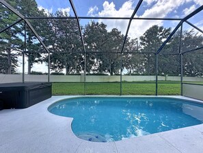 A covered outdoor swimming pool with a view of a grassy area and trees. - Luxury 5BD 3.5BA Pool Home in Windsor Palms Resort (Kissimmee)