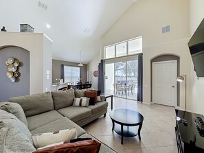 A spacious living area with a large sofa, a coffee table, and a dining area with chairs and a table. - Luxury 5BD 3.5BA Pool Home in Windsor Palms Resort (Kissimmee)
