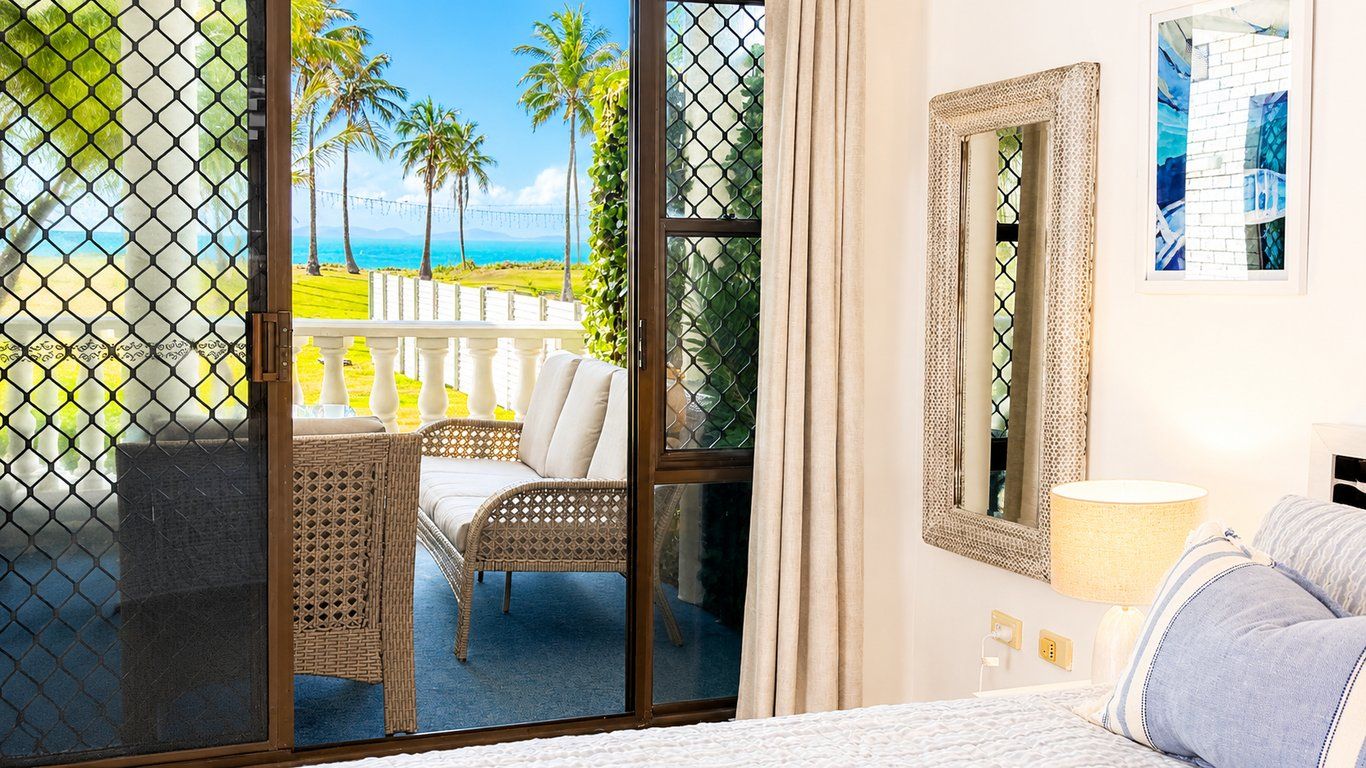 A hotel room with a balcony, a bed, a chair, and a painting on the wall.
