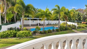 A pool area with a white fence, palm trees, and a clear blue sky. - **Between Two Blues – Beachfront Bliss in Yeppoon** (Yeppoon)