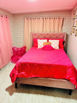 A bed with a red quilt, a tufted headboard, and a pink accent pillow. - The Pink Rooster Casita (Tucson)