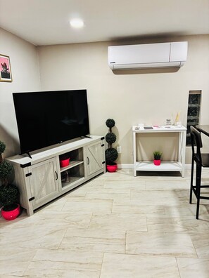 A living room with a flat-screen TV on a wooden cabinet, a white console table with decorative items, and a potted plant. - The Pink Rooster Casita (Tucson)