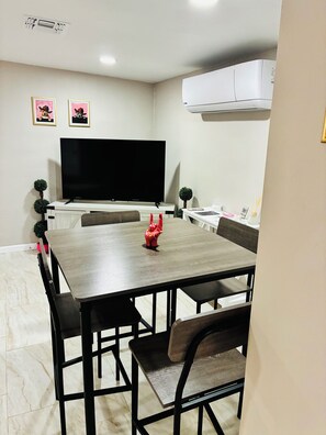 A dining area with a rectangular table, black chairs, a flat-screen TV, and two framed pictures on the wall. - The Pink Rooster Casita (Tucson)