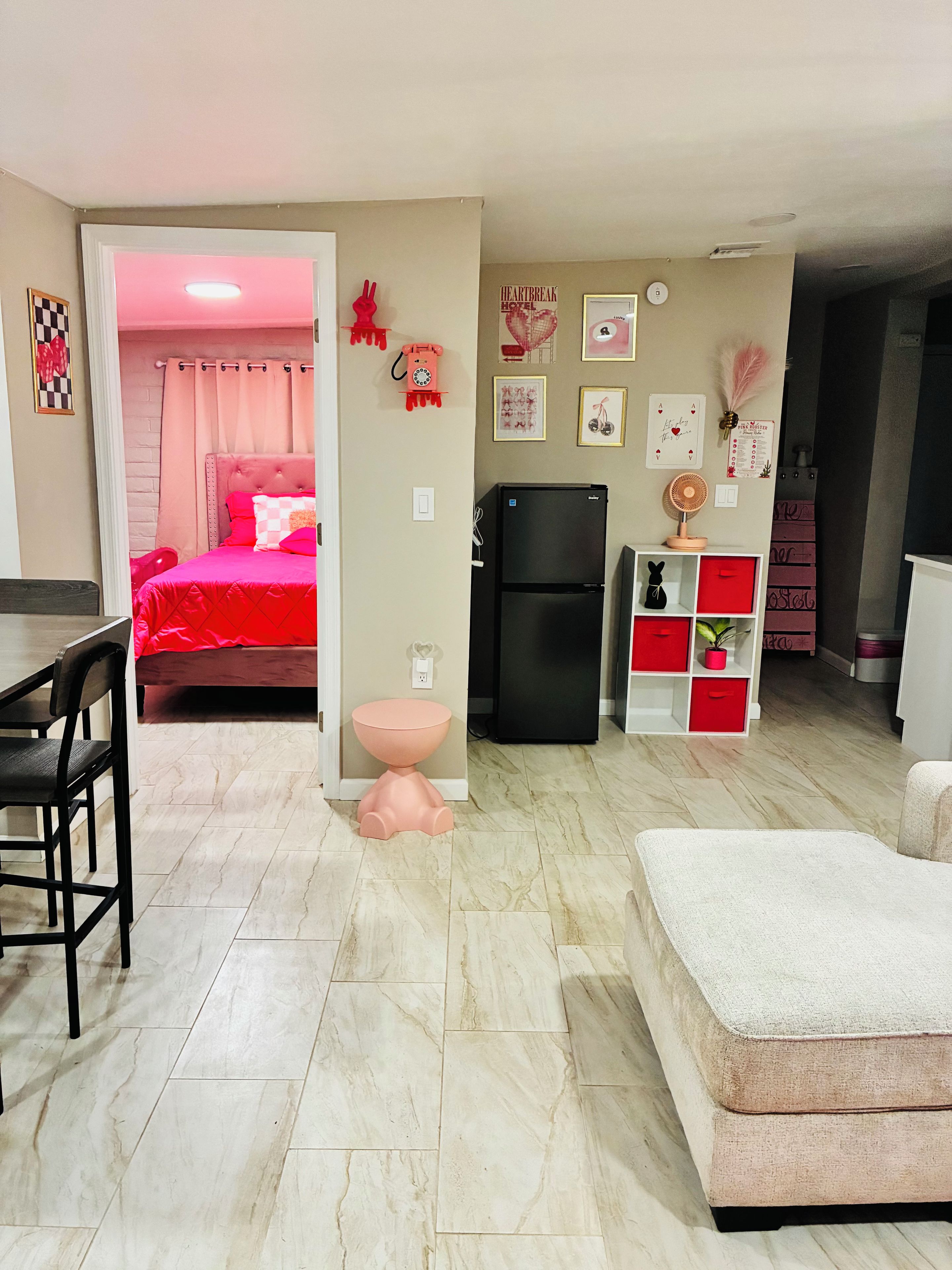 Ein Hotelzimmer mit einem Bett, einem Esstisch, einem Kühlschrank, einem kleinen rosa Tisch und einem weißen Sofa.