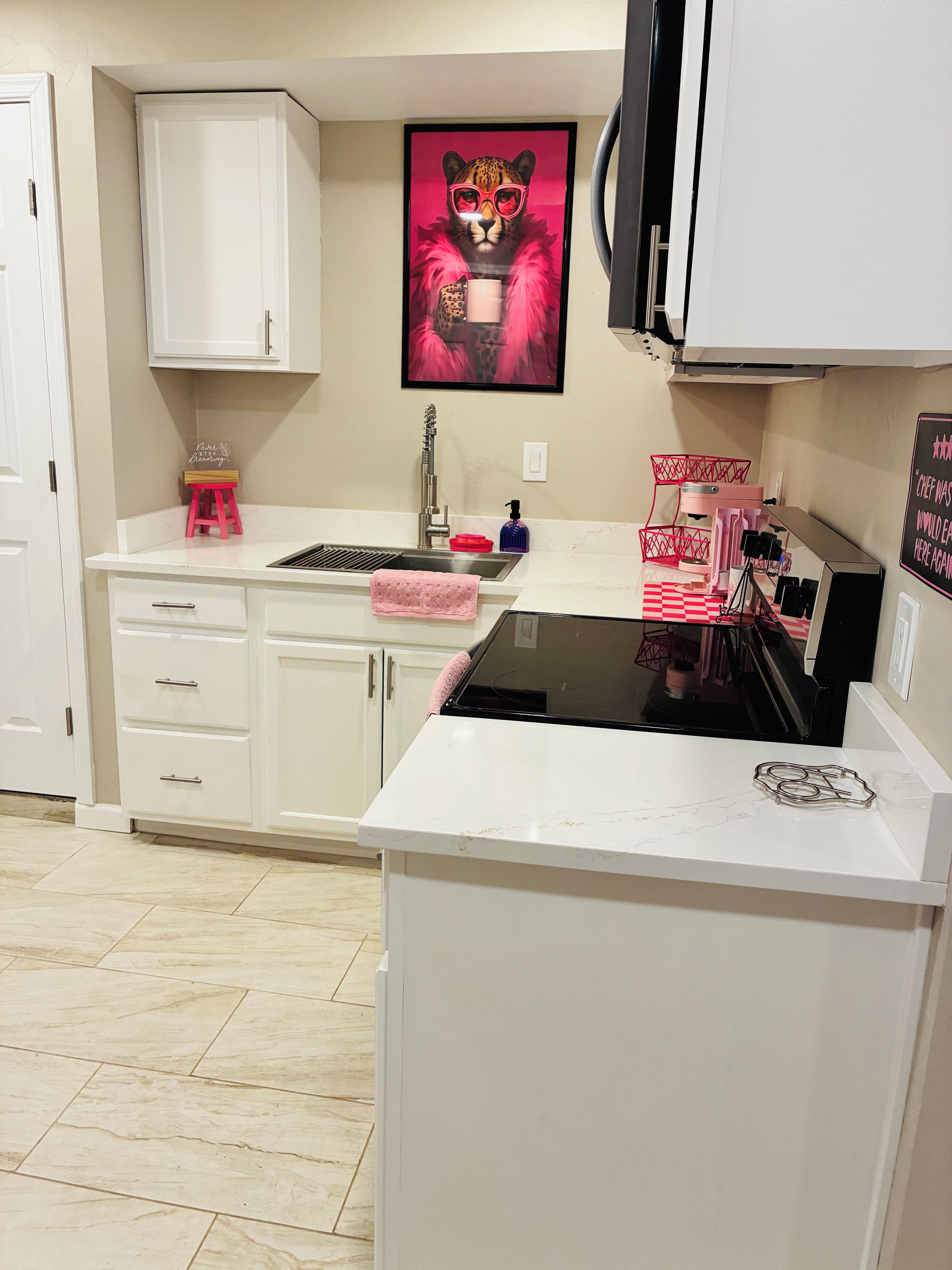 A kitchen with white cabinets, a stainless steel sink, a pink towel, and a framed picture of a leopard.