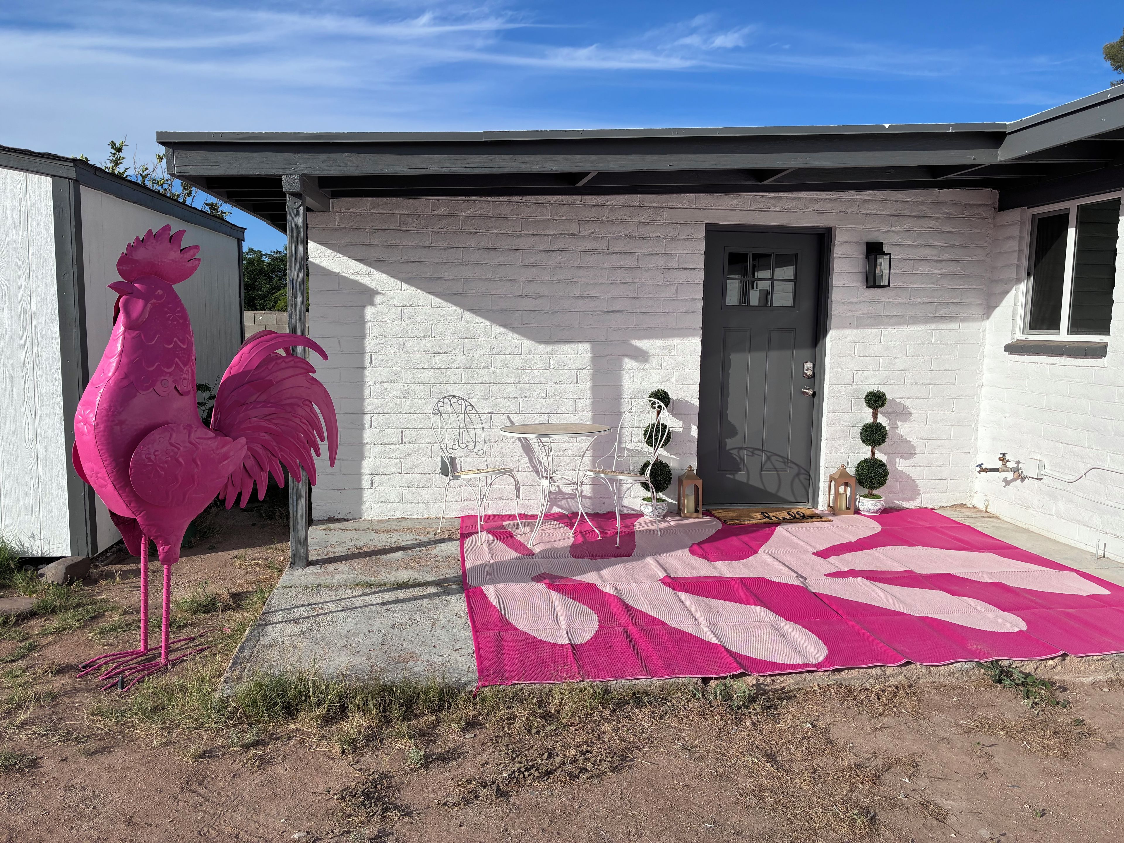 Ett hus med en vit tegelstensfasad, en grå dörr och en rosa tupp som pryder huset.