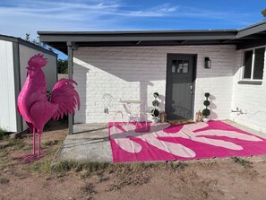 A house with a white brick exterior, a gray door, and a pink rooster decoration. - The Pink Rooster Casita (Tucson)