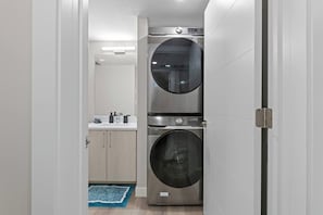 Una sala de bugaderia amb dues rentadores superposades i un lavabo amb articles de tocador.
